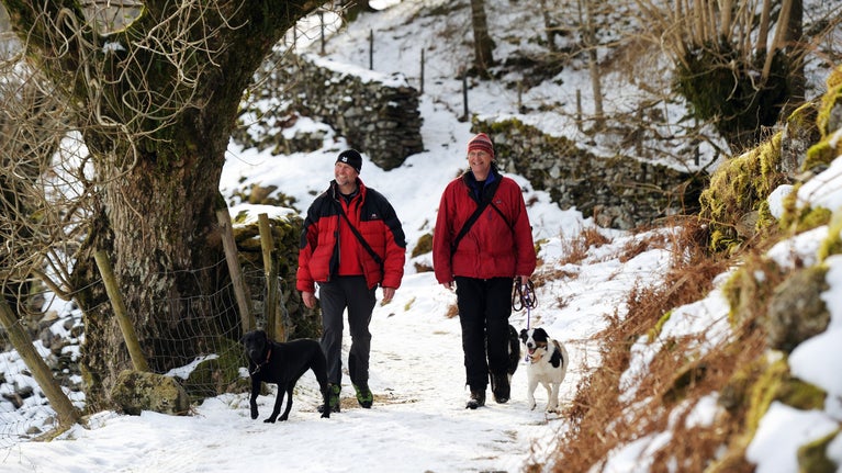 Two visitors walk along a snow covered track with their dogs in the hamlet of Watendlath in Cumbria